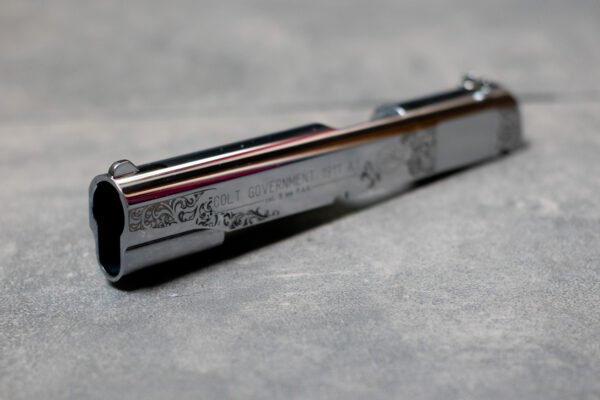 Detailaufnahme einer Lasergravur auf einem Colt 1911 Schlitten mit feinen Ornamenten auf verchromter Oberfläche